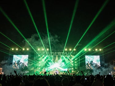Wide stage setup at night with heavy smoke, green spotlights piercing through, festival energy
