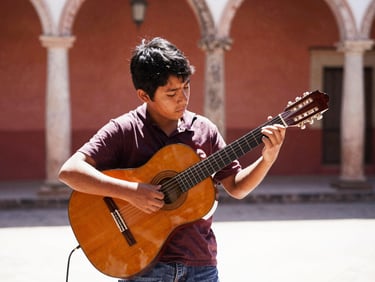 A young person playing a traditional acoustic guitar in a bright courtyard in Jalisco, warm sun, authentic moment.