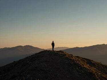 Solitary figure in a contemplative mountain landscape at golden hour, expansive sky, muted navy and gold tones, shallow depth of field, 35mm.