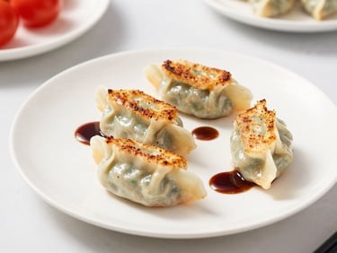 Three golden pan-seared gyoza dumplings arranged elegantly on a white plate, small drizzle of dark reduction, bright daylight