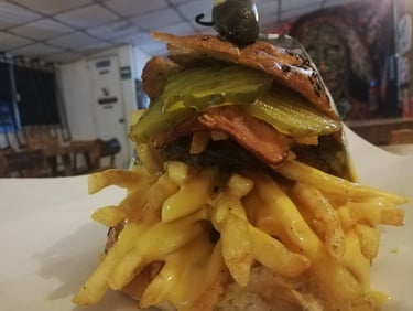 Hamburguesa gourmet con queso y tocino, cubierta con pepinillos y una generosa porción de papas.