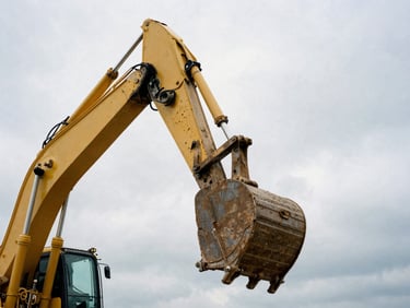 Low-angle shot of a large yellow excavator bucket against a cloudy sky, showing hydraulic details, overcast daylight, gritty desaturated tones, industrial documentary photography, 35mm film grain
