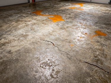 Gritty, cracked concrete garage floor with oil stains and visible wear under dim light