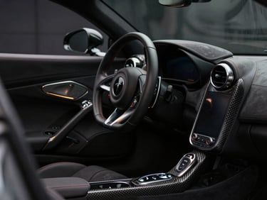 Pristine interior of a luxury sports car showing the leather steering wheel and carbon fiber console, soft ambient dashboard lighting, shallow depth of field