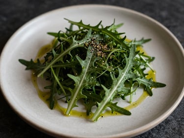 Minimalist salad of bitter greens on a cream ceramic plate, olive oil drizzle, visible cracked black pepper