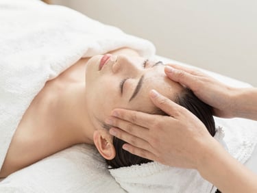 Close-up of gentle hands performing a facial massage on a client, soft diffused lighting, white linen