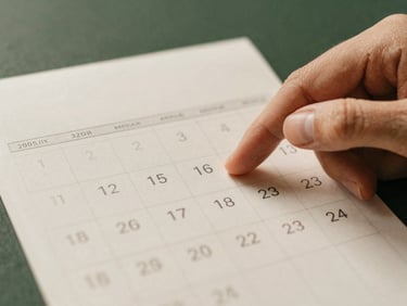 A calendar with a marked date, hands pointing to it, warm natural light, muted background, warm editorial photography