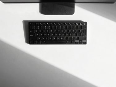 Straight-on flat lay of a minimalist workspace, sleek black keyboard on a stark white desk, sharp geometric shadows, high-contrast monochrome photography.