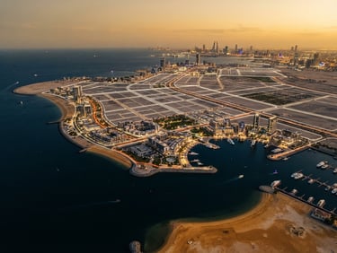Wide-angle architectural survey of prime coastal land in Bahrain at golden hour, clean geometric masterplan lines overlaid, high-contrast, premium 35mm photography.