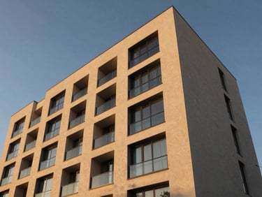 Low angle architectural photograph of J Suites exterior, modern clean lines against a golden-hour sky, warm sand tones, sharp focus, 35mm