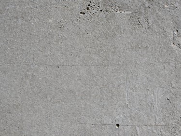 Extreme macro detail of raw, textured concrete showing fine grain and air pocket imperfections, overcast diffused lighting.