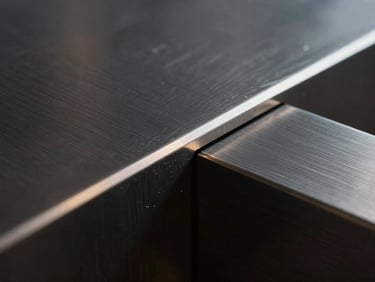 Macro shot of dark architectural steel with fine brushed lines, high-contrast side lighting highlighting the metallic edge.