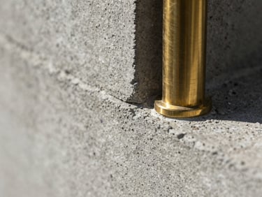 Extreme macro close-up of raw board-formed concrete and brushed brass joint under harsh side light, revealing rich tactile texture and precise material grain.