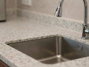 Close-up shot of the same kitchen counter completely cleared, with a sparkling polished faucet and dust-free granite countertops.