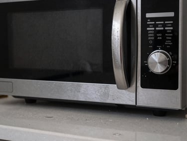 Close-up shot of a messy kitchen counter with water spots on the stainless steel faucet and dust on the microwave surface.
