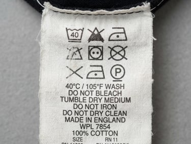 Extreme close-up of a vintage garment care label, stark white cotton tag with black printed text, flat-lay overhead shot, neutral grey studio background, sharp focus