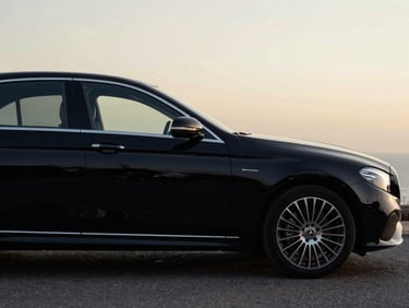 Side profile of a black Mercedes-Benz E-Class sedan under soft studio lighting, deep black metallic paint, high contrast.