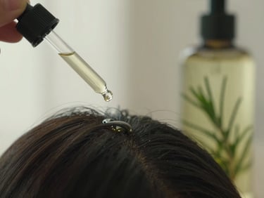 Close-up of a dropper dispensing rosemary oil onto a scalp, next to a bottle of rosemary-infused shampoo, soft diffused window light, vertical composition.