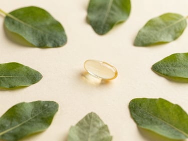 Elegant flat lay of clear botanical capsules and raw green leaves on an ivory background.