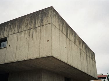 A dramatic angle of a brutalist concrete facade in Bogotá, overcast sky, soft shadows, architectural scale, 35mm film