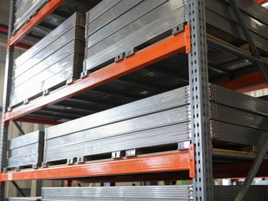 Low-angle industrial photography of heavy-duty steel shelving units stacked with heavy cargo, bright workshop light reflecting off clean welds and dark metal surfaces, sharp focus