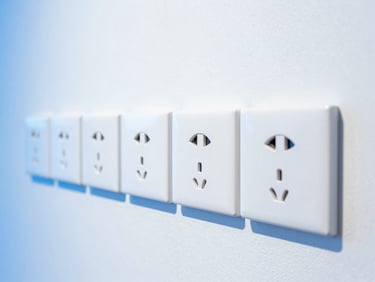 Arrangement of modern electrical switches and sockets on a clean white wall, with a subtle blue glow, bright cool daylight, bold blue and white tones, crisp clean focus, 35mm lens