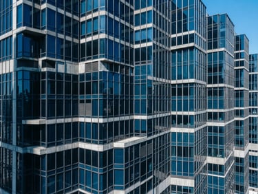 High-angle architectural photography of a modern corporate office building facade, crisp daylight with sharp geometric shadows, cool concrete and deep blue tones, technical grid overlay, 35mm