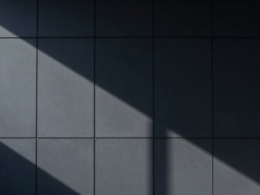 Abstract geometric shadows on a modern office wall, minimalist corporate photography, cool diffused daylight, deep navy and slate tones, architectural symmetry, 35mm lens