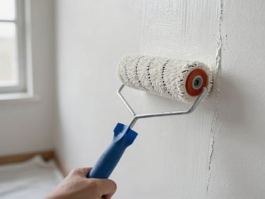 Close-up of a paint roller moving across a freshly prepared wall, natural light from a window to the left, smooth white paint covering the surface in a single even pass, drop cloth visible on the floor below