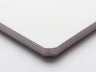 Macro close-up of high-fidelity printed business cards showing paper texture and sharp embossed edges, bright studio lighting, white background