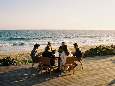 A wide-angle golden hour shot of remote workers collaborating on a sunlit wooden deck overlooking the ocean, warm side-lighting, 35mm film texture.