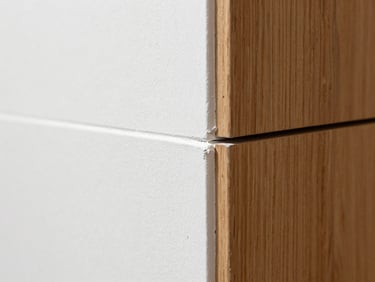 Macro architectural detail of a perfectly finished wall joint where smooth white plaster meets a warm oak panel, clean shadow gap, precise craftsmanship.