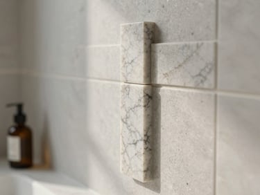 Fotografia de detalhe de uma junta de pedra mármore perfeitamente alinhada numa parede de casa de banho moderna, luz natural suave lateral revelando a textura precisa e o rigor da execução.