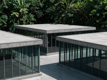Wide architectural shot of interlocking concrete and glass pavilions, sharp natural daylight, high contrast, deep forest green shadows, 35mm lens