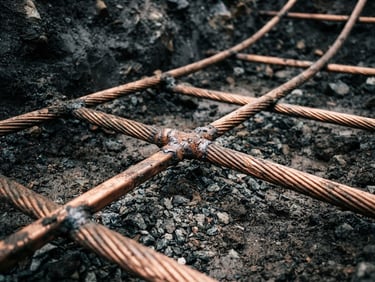 Close-up macro shot of a heavy-gauge copper grounding grid laid in a utility substation trench, high-contrast overcast daylight, sharp focus, 35mm