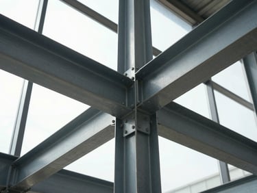 Wide environmental shot looking up along a structural steel column-and-beam connection in a commercial interior, bolted connection plate in sharp focus, diffused natural daylight from a high clerestory window revealing the steel's surface preparation