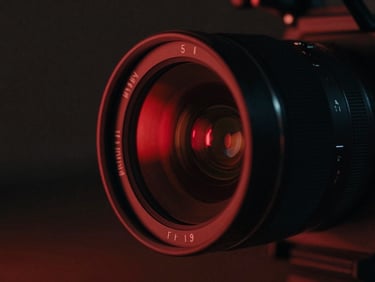 Cinematic close-up of an anamorphic camera lens, low-key lighting with red neon reflections, high contrast chiaroscuro, 35mm film grain, 21:9 aspect ratio.
