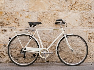 A vintage Peugeot road bicycle, fully restored, painted in white and gold, parked against a warm Bordeaux stone wall, soft natural daylight, 35mm
