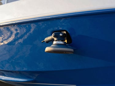Close-up of a rotary polisher on a boat hull, showing a before-and-after reflection line, golden hour sunlight, deep blues