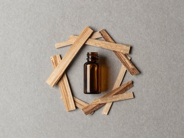Overhead flat-lay of raw cedarwood chips and a small amber glass vial on a textured warm-grey background, soft directional light, minimalist.