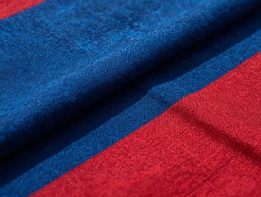 Close-up of hand-woven indigo and crimson textile textures, dramatic shadows, natural sunlight.
