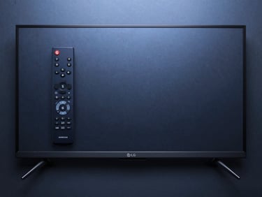 Flat-lay top-down shot of a Samsung Smart TV remote and a sleek LG television side by side on a dark matte surface, lit with cool blue studio light from above, minimalist and clean