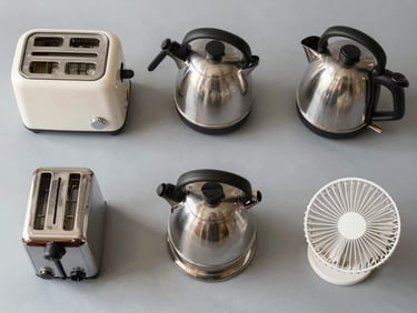 Flat-lay overhead shot of household appliances — a toaster, kettle, and small fan arranged on a neutral gray surface, bright studio lighting, no branding visible, clean product-condition context