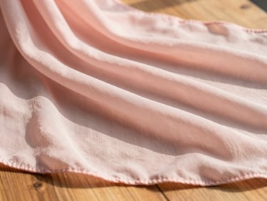 Close-up of soft pastel pink chiffon georgette fabric draping over a wooden table, warm morning daylight, shallow depth of field