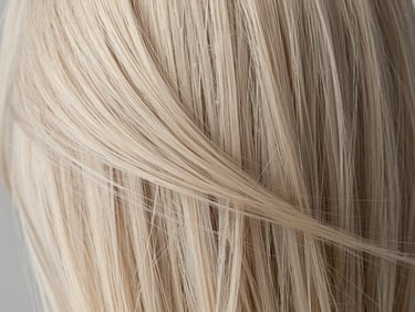 Extreme close-up of freshly colored platinum blonde hair strands in soft natural light, showing color depth and smooth texture
