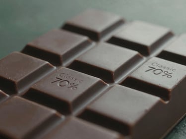 Close-up of a matte dark chocolate bar, Classic 70%, breaking cleanly, rich cacao-husk bronze tones, soft misty natural light, shallow depth of field