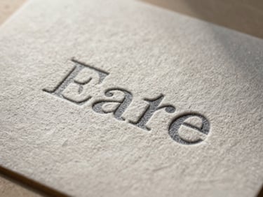 Macro close-up of heavy embossed cotton paper stock with a deep letterpress brand identity, casting structural shadows under low-angle natural light.
