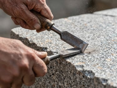 Extreme close-up of weathered hands holding a steel chisel and striking a raw granite block, high-contrast side lighting highlighting the physical texture and flying stone dust.