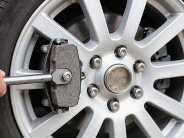 Close-up of a mechanic replacing brake pads on a clean wheel hub, precision tools visible, bright natural daylight, sharp commercial photography.