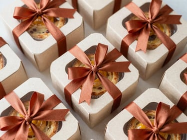 Overhead flat-lay of premium cardboard treat boxes tied with terracotta silk ribbon, revealing artisanal bakes inside